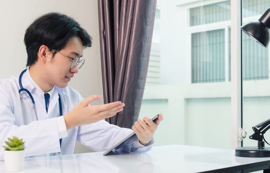 Happy Asian young doctor handsome man smile wear glasses use modern smart digital tablet computer explain patients symptoms of illness on desk at hospital office, Technology Healthcare And Medicine