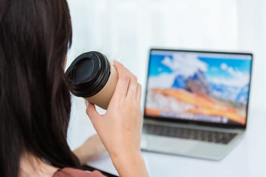 Work from home, Back of Asian young businesswoman video conference call or facetime meeting online hold coffee cup on front laptop computer quarantines disease coronavirus or COVID-19 at home office