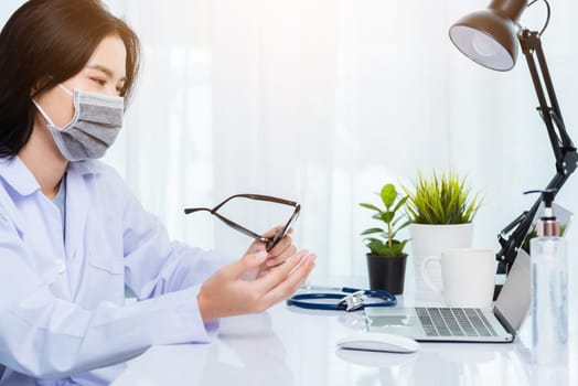 Asian young beautiful woman doctor wear face mask protective video call conference online raise hand explain to patients on laptop computer quarantines disease coronavirus or COVID-19 at hospital