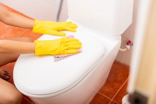 Woman cleaning toilet seat by pink cloth wipe restroom, female wearing yellow rubber gloves she sitting and clean the bathroom, Housekeeper healthcare concept