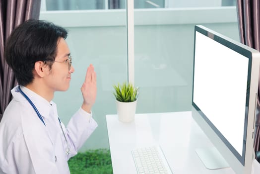 Asian young handsome doctor man wearing a doctor's dress and stethoscope video conference call or facetime raise hand say hello to patient he smiling on desk at hospital office, Health medical care