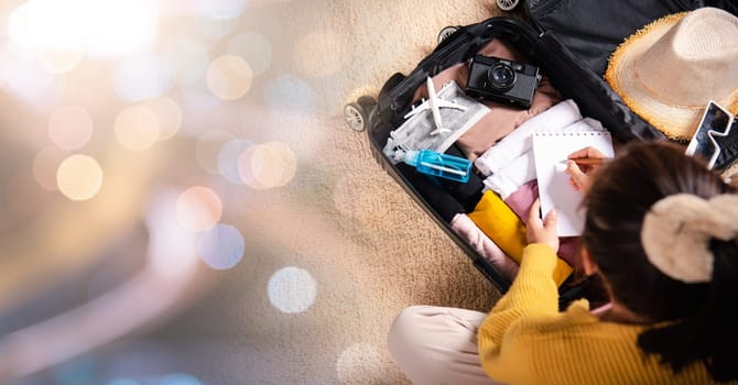 Making check list of things to pack for travel. Woman writing paper take note and packing suitcase to vacation writing paper list sitting on room, prepare clothes into luggage, Travel vacation travel
