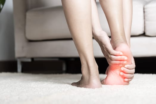 Foot pain, Asian woman standing feeling pain in her foot at home, female suffering from feet ache use hand massage relax muscle from soles in home interior, Healthcare problems and podiatry medical