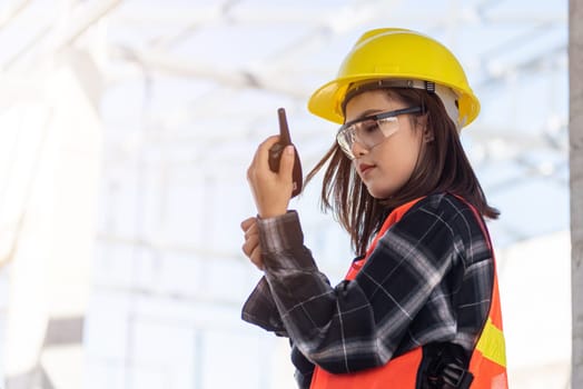 Asian engineer foreman architect worker woman working at building construction site talking with radio, engineering hold radio discuss operate and control worker employee to building construction