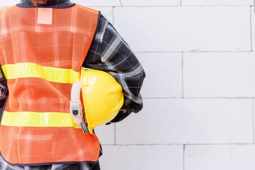 Back view of engineer, architect, supervisor worker wear reflective clothing for the safety of the work operation hold safety helmet in vest standing at wall building construction site