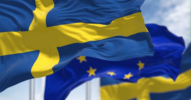 Detail of the national flag of Sweden waving in the wind with blurred european union flag in the background on a clear day. Democracy and politics. European country. Selective focus.