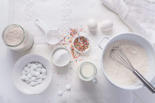 Baking background with flour, eggs, sugar sprinkles, kitchen tools, utensils in white