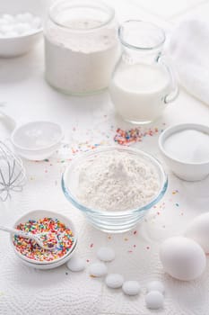Baking background with flour, eggs, sugar sprinkles, kitchen tools, utensils in white