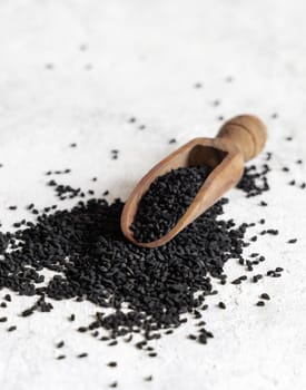 Wooden scoop of Indian spice Black cumin (nigella sativa or kalonji) seeds close up on white table. Traditional asian medicine, healthy eating, vegetarian and vegan food concept