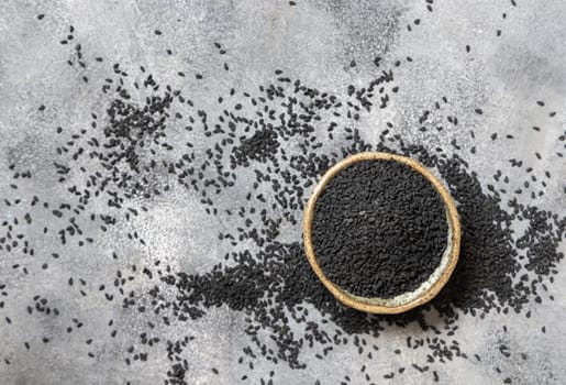 Indian spice Black cumin (nigella sativa or kalonji) seeds in bowl on grey table top view with copy space. Traditional medicine, healthy and vegetarian food concept.