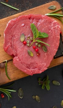 Raw beef fillet steak on wooden board on dark table top view. Portioned filet mignon with spices and herbs. Concept of summer food