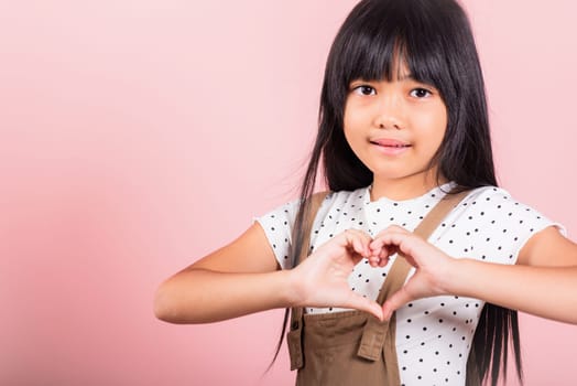 Asian little kid 10 years old showing heart sign at studio shot isolated on pink background, Happy child girl making heart shape gesture with hands, Cheerful kid, Valentine day