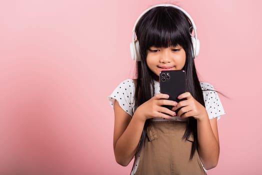 Asian kid 10 years enjoying listening music from mobile phone wear wireless headset at studio shot isolated on pink background, Happy child girl lifestyle use smartphone listen music with headphones