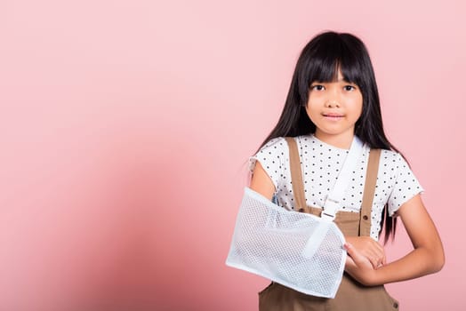 Arm broken. Asian little kid 10 years old hand bone broken from accident with arm splint at studio shot isolated on pink background, Happy child girl accident insurance and extreme sports speed