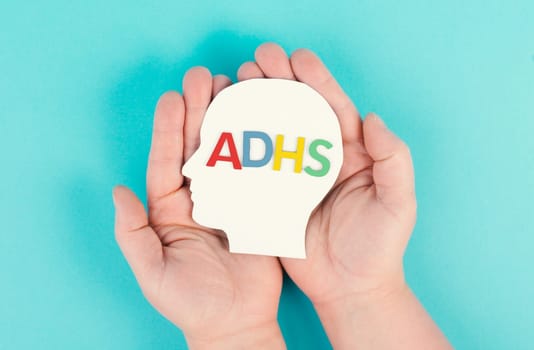Hands holding a head with the german word ADHS which means attention deficit hyperactivity disorder, ADHD symptom, mental health