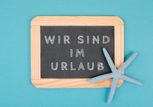 We are on vacation is standing in german language on the chalkboard with a sea star, holiday background, time out in summer, hot weather, advertising and marketing concept