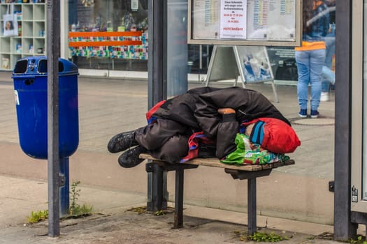 WETZLAR, GERMANY - APRIL 23, 2022: Homeless man lies on a seat of a public bus stop