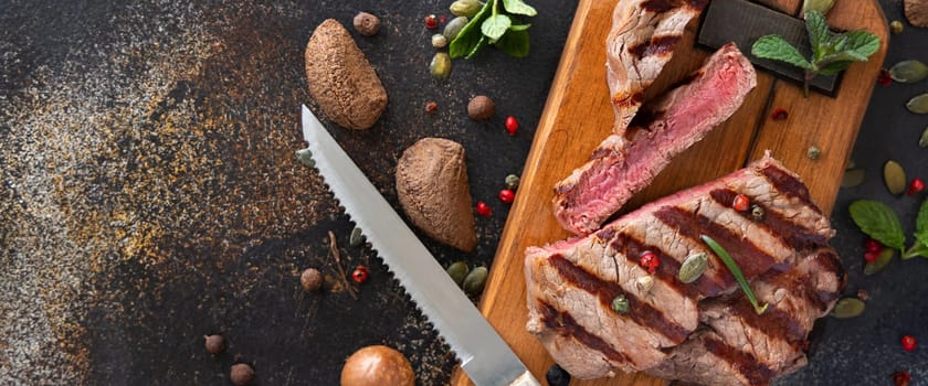 Grilled beef fillet steaks on dark table close up with copy space. Portioned filet mignon with spices and herbs. Concept of summer food, meat eaters.