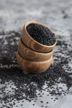 Indian spice Black cumin (nigella sativa or kalonji) seeds in wooden bowls on grey table close up. Traditional medicine, healthy and vegetarian food concept.