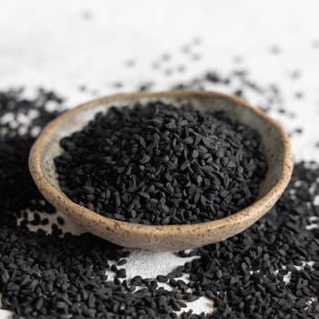 Indian spice Black cumin (nigella sativa or kalonji) seeds in bowl on grey table close up. Traditional medicine, healthy and vegetarian food concept.