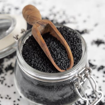 Indian spice Black cumin (nigella sativa or kalonji) seeds glass jar with a wooden scoop, close up. Traditional asian medicine, healthy and vegetarian food concept