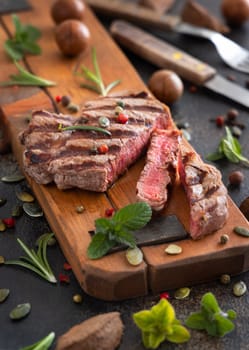Grilled beef fillet steaks on dark table close up. Portioned filet mignon with spices and herbs. Concept of summer food, meat eaters.