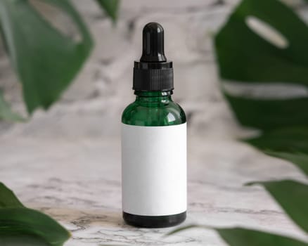 Dropper Bottle on tropical monstera leaf on white marble table close up. Brand packaging mockup. Aromatic oil, skincare beauty product, cream or serum. Natural herbal cosmetics concept..