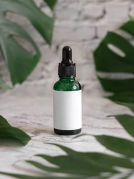 Dropper Bottle on tropical monstera leaf on white marble table close up. Brand packaging mockup. Aromatic oil, skincare beauty product, cream or serum. Natural herbal cosmetics concept..