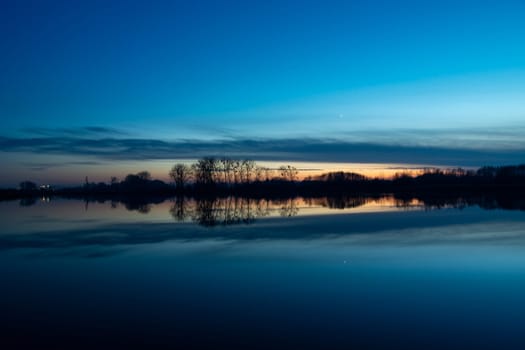 Reflection of trees and clouds in the lake water, sunset view