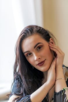 Portrait of attractive dark haired girl posing with hands on chin. Vertically.