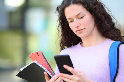 Serious student reading phone content in a campus