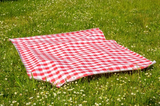 Red picnic blanket. Red checkered picnic cloth on a flowering meadow with daisy flowers. Beautiful backdrop for your product placement or montage.