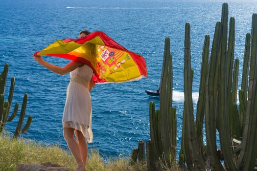 Young woman with Spain flag on a rock in the background the blue sea