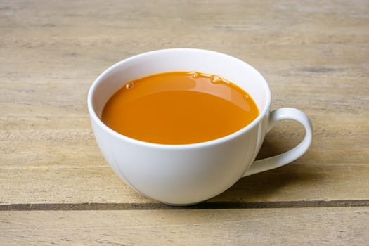 Hot milk tea in a white cup on wooden table