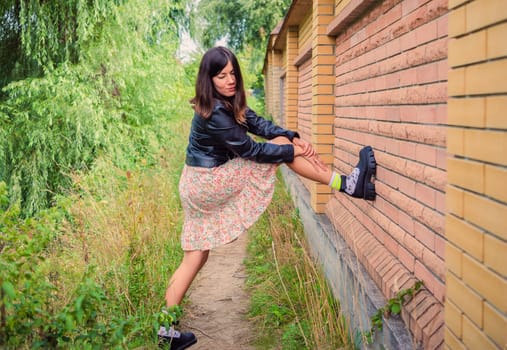A young brunette girl stands with her foot on a brick wall in the park