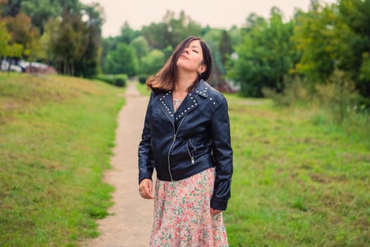 a beautiful young woman stands on a path in the park, covering half her face with her hair