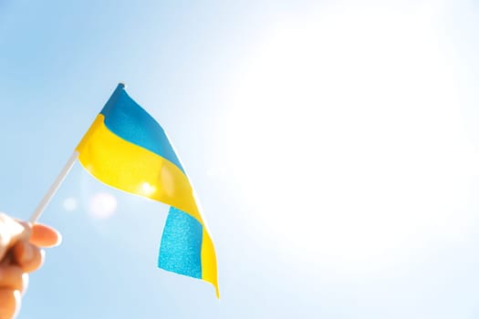 Human hand holding large bicolor yellow blue Ukrainian state flag, national symbol fluttering, waving in wind against blue sky on sunny day. Ukraine Independence Constitution Day, National holiday