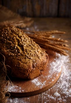 Homemade bread loaf and wheat ears on rustic wooden background