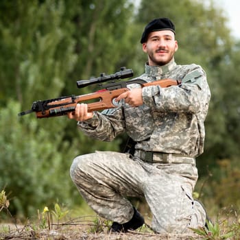 The smiling soldier in military uniform is holding a crossbow weapon outdoors.