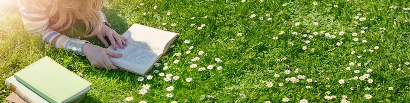 Young woman lying on the field and reading some books. Concept of hobby, relaxing and studying.