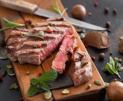Grilled beef fillet steaks on dark table close up. Portioned filet mignon with spices and herbs. Concept of summer food, meat eaters.
