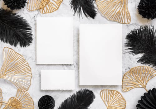Blank cards on marble table near black feathers and golden leaves top view. Wedding set mockup. Elegant femminine suite with paper cards, flat lay