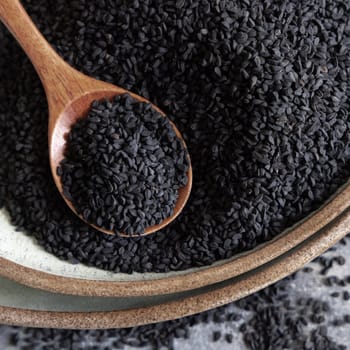 Plate of Indian spice Black cumin (nigella sativa or kalonji) seeds on grey table with a wooden spoon, top view. Traditional asian medicine, healthy and vegetarian food concept