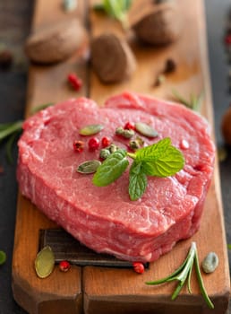 Raw beef fillet steak on wooden board on dark background close up. Portioned filet mignon with spices and ingredients. Concept of summer food