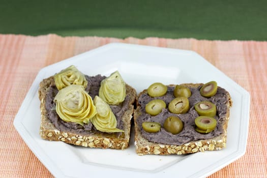 Food snack dinner of sprouted grain bread vegetarian bread with black bean hummus, artichoke hearts and garlic stuffed olives. Vegan meal of bread, black bean hummus, artichoke hearts, garlic olives