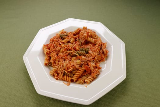 Spinach, carrot and tomato semolina and durum wheat tri-color rotini vegetable pasta with shredded chicken and tomato sauce on a plate. Vegetable rotini pasta mixed with chicken meat and tomato sauce.