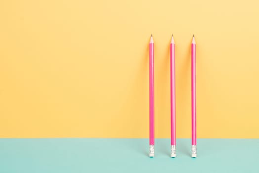 Pink pencils on a yellow and blue background, minimalism, creative, surreal and education concept, copy space for text, pastel colored wall