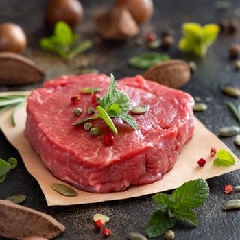 Raw beef fillet steaks on dark table close up with copy space. Portioned filet mignon with spices and herbs. Concept of summer food, meat eaters.