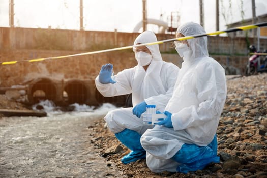 Ecologist sampling water from the river with test tube, Scientist or Biologist in a protective suit and protect mask collects sample of waste water from industrial for analyze, problem environment
