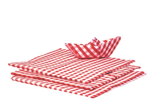 Closeup of a stack of red checked paper napkins and a folded paper ship isolated on a white background. Clipping path. Macro. Stacked towel or tablecloth.